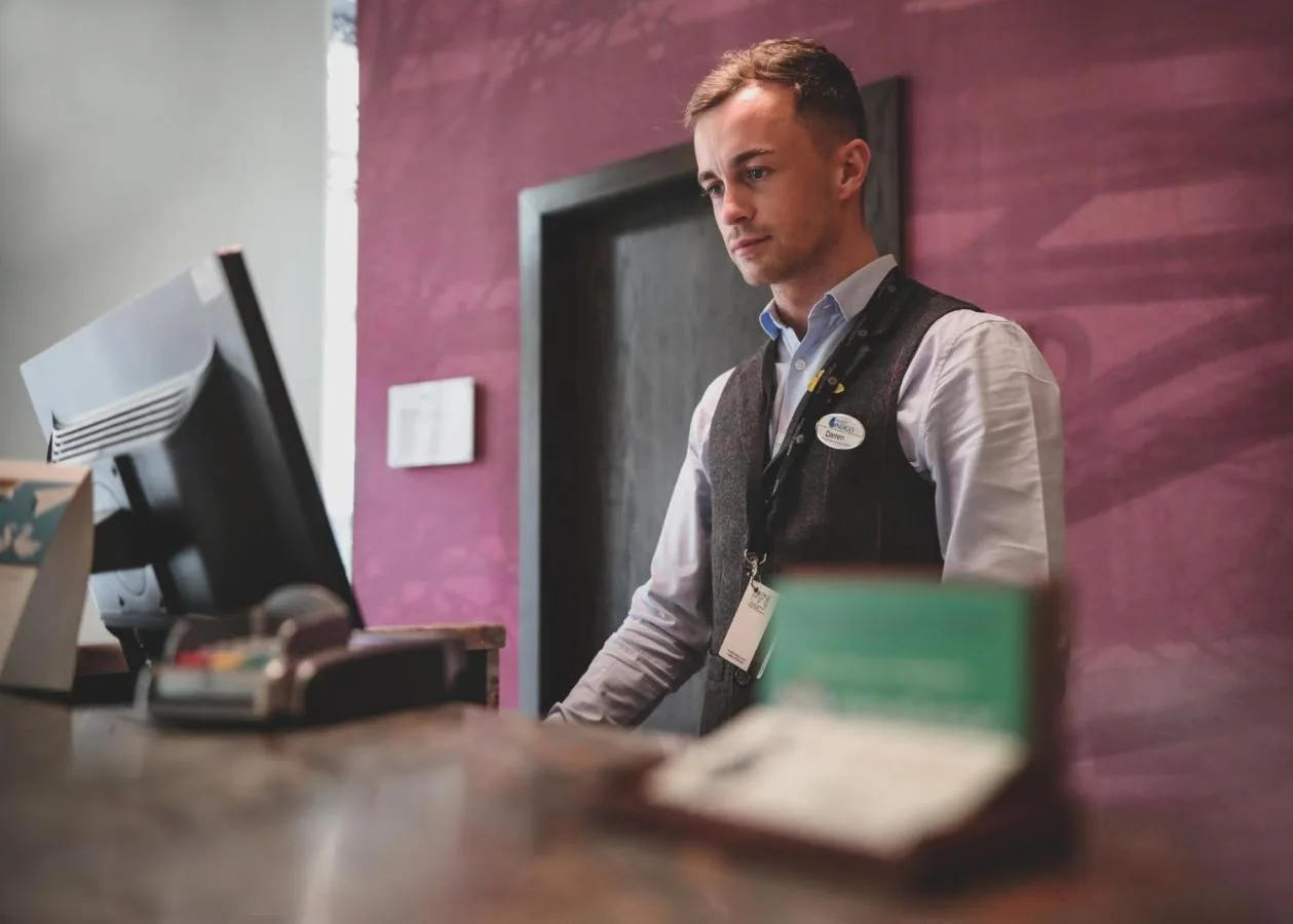 a man standing in front of a desk with a computer at Hotel Indigo Glasgow by IHG in Glasgow