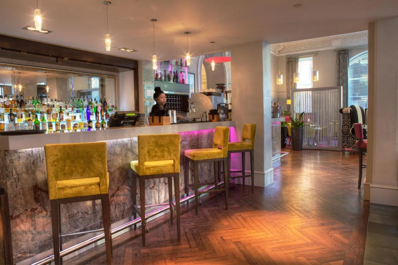 a bar with yellow chairs and a woman in the background at Hotel Indigo Glasgow by IHG in Glasgow